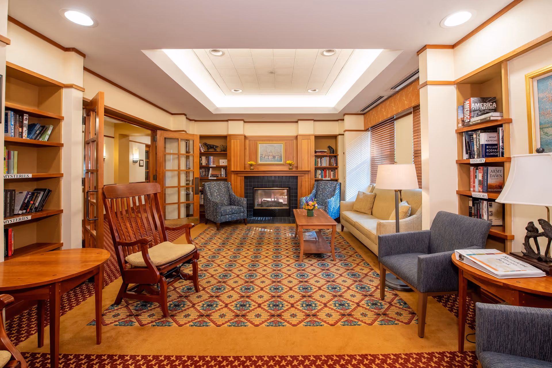 Cozy common living room with a fireplace, sofas and armchairs, bookshelves, and a patterned rug.
