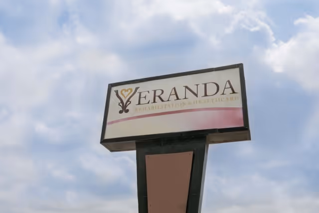 A roadside sign reading "Veranda Rehabilitation & Healthcare" against a cloudy sky.