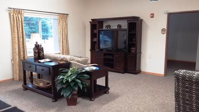 Comfortable living room with a sofa, side tables, potted plant, and a large wooden entertainment center with a TV.
