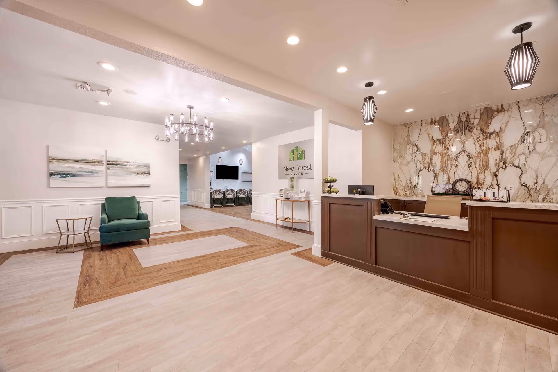 Reception area of New Forest Haven featuring a wooden front desk with a marble backdrop, two pendant lights hanging from the ceiling, a green armchair with a small side table, a chandelier, and a hallway leading to a room with chairs and a wall-mounted TV.