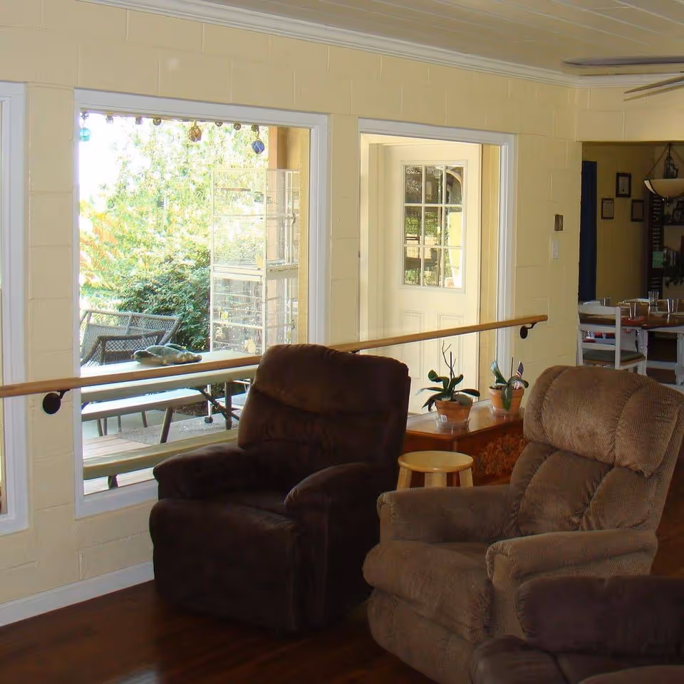 Two upholstered recliners in a bright common living area with large windows looking out to a patio.