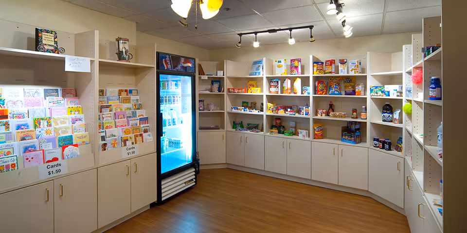 Small indoor convenience shop with shelves of greeting cards, snacks, and a refrigerated drink cooler.
