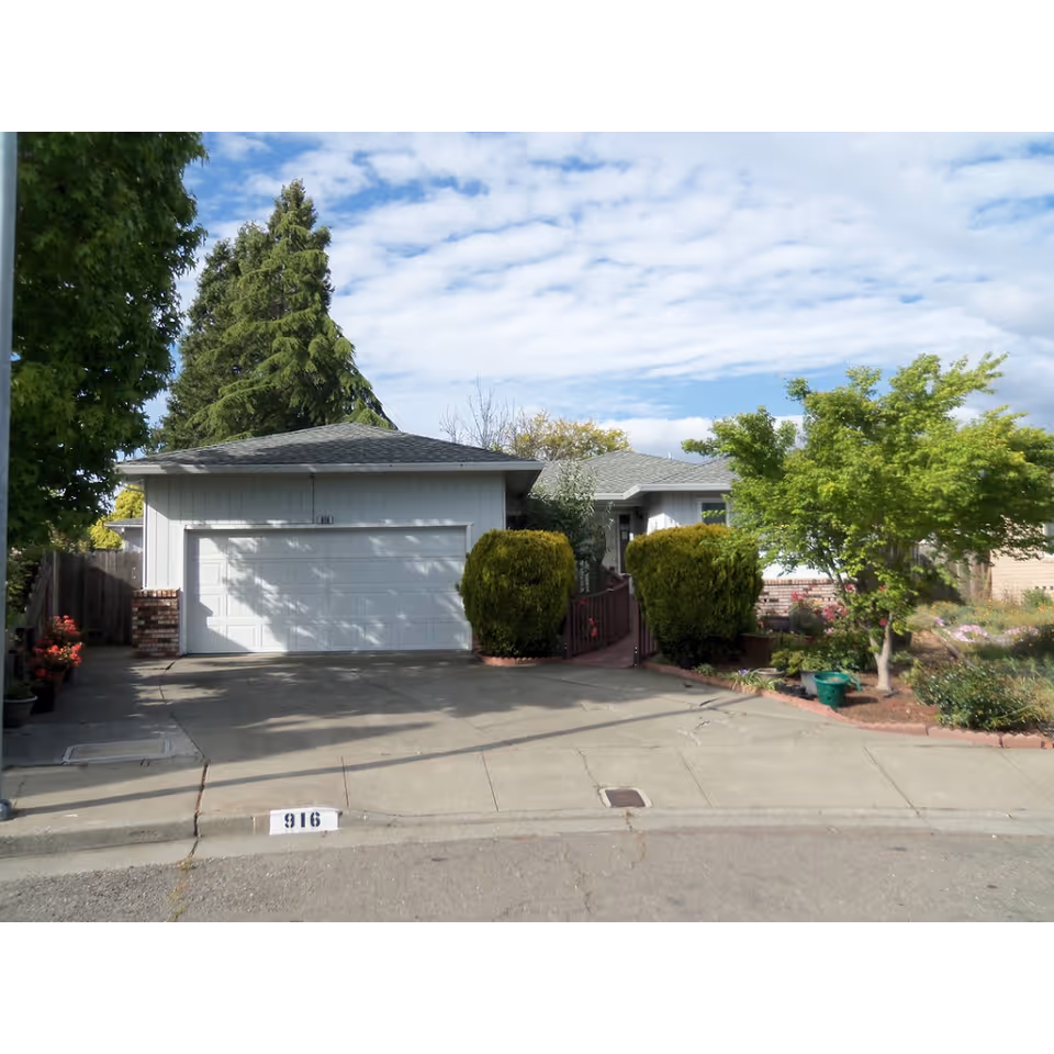 Front exterior of a single-story house with a two-car garage, driveway, and landscaped front yard.