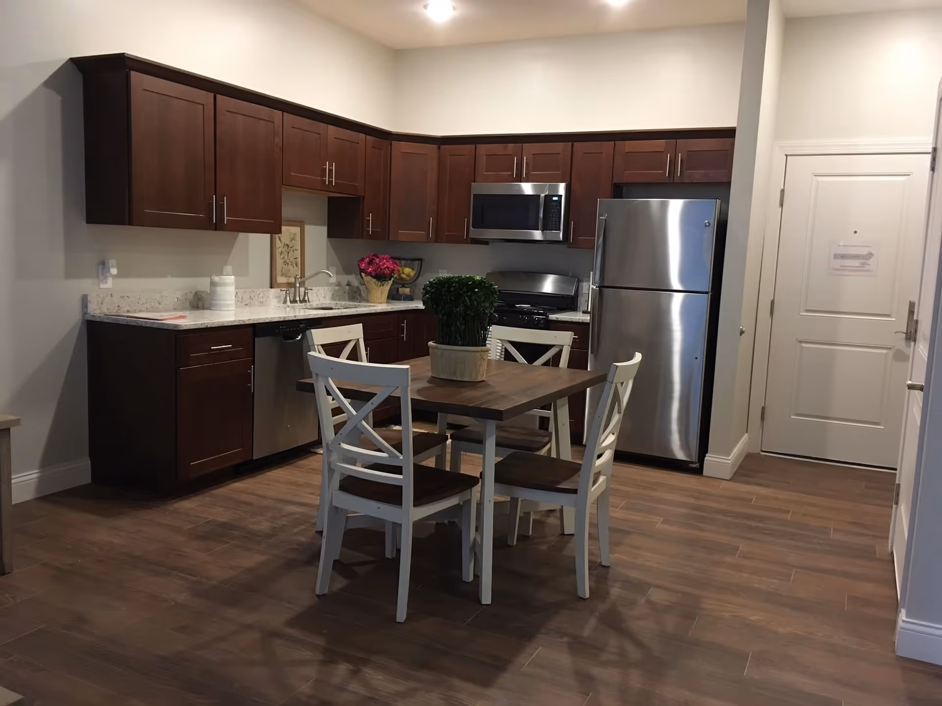 Open kitchen with dark wood cabinets, stainless steel appliances and a small wooden dining table with four chairs.