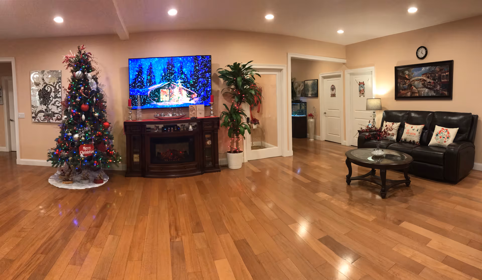 Spacious living room with hardwood floors, a decorated Christmas tree, a wall-mounted TV and fireplace console, and a leather sofa with a coffee table.