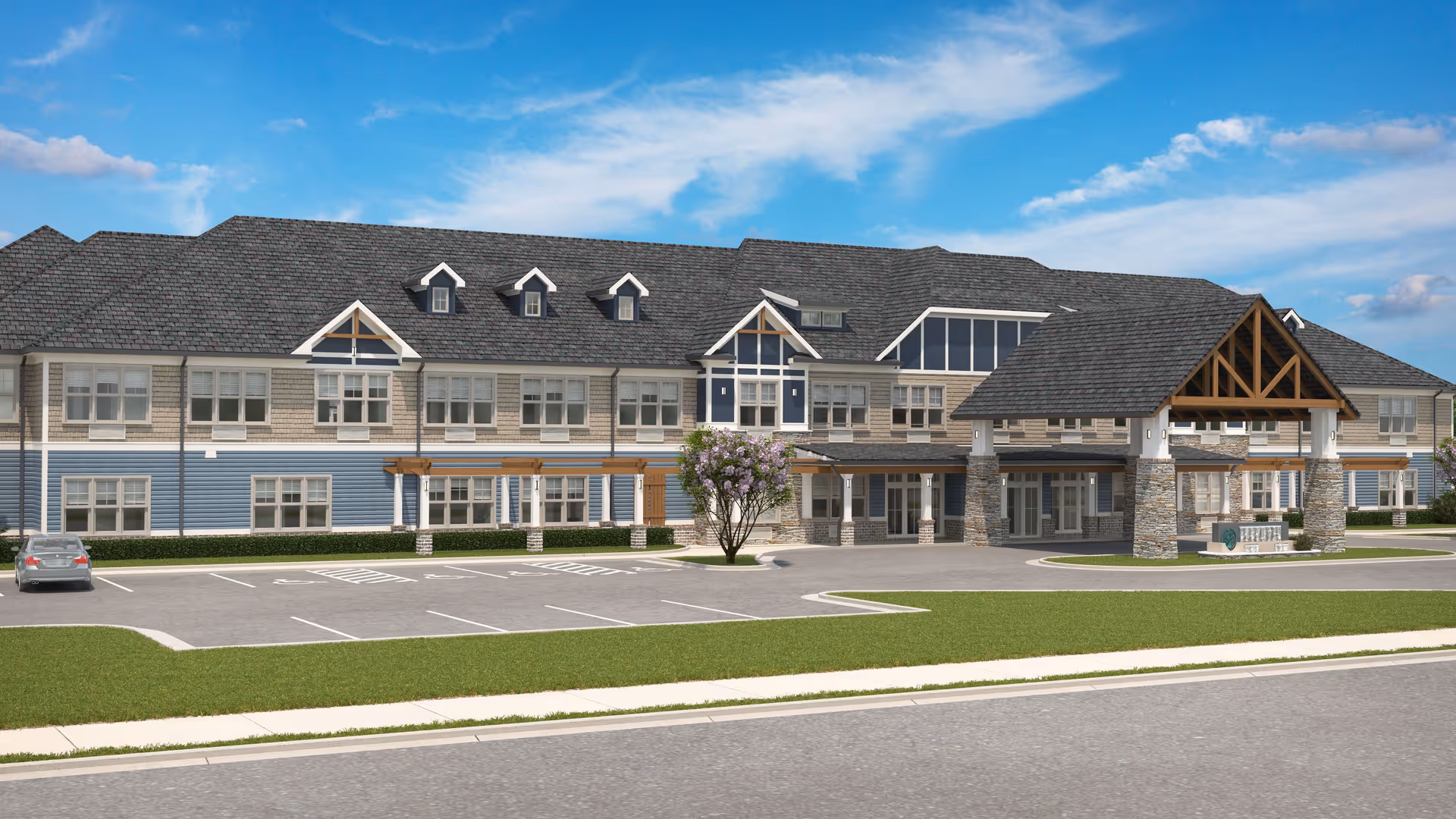 Exterior view of Oaks at Aiken, a large two-story building with a covered entrance supported by stone pillars, multiple windows, a parking lot with a single car, green lawn, and a partly cloudy blue sky.