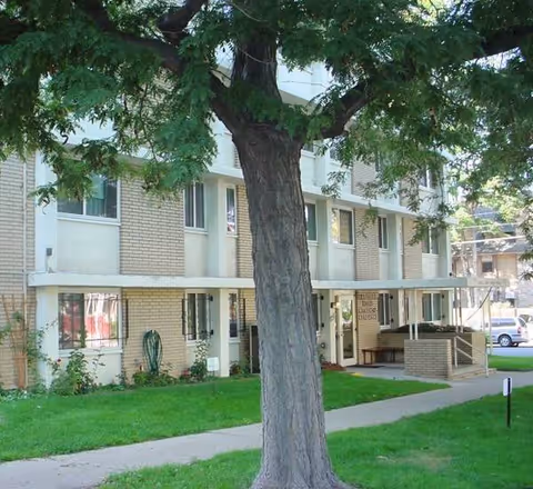 Exterior view of a multi-story senior living building with a large tree in front.