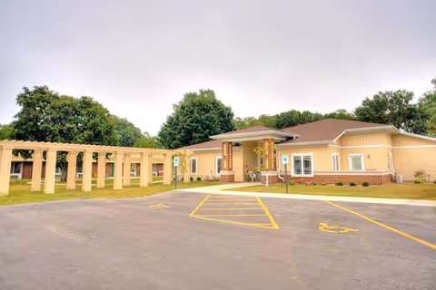 Exterior view of a yellow senior living facility with a covered entrance and parking.
