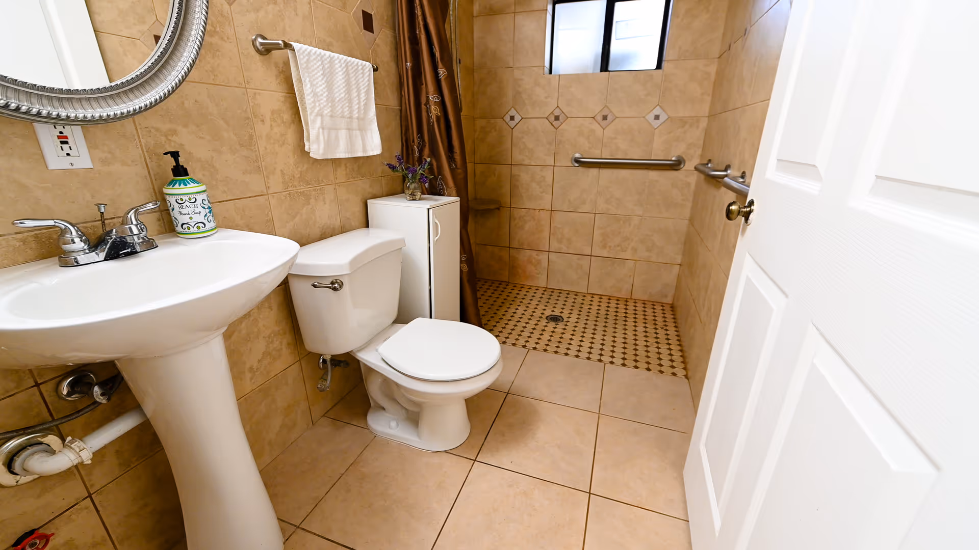 Tiled bathroom with a pedestal sink, toilet, and a walk-in shower with grab bars.