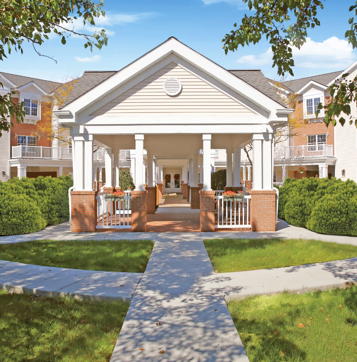 Front exterior view of The Inn at Walker Mill showing a covered walkway with white columns and brick bases, surrounded by green bushes and grass, with a clear blue sky above.