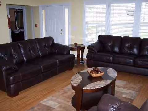 A living room with dark leather sofas, a coffee table, and large windows.