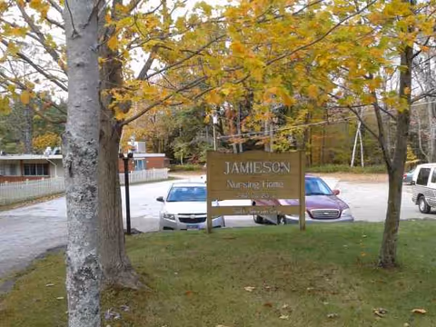 Exterior view of Jamieson Nursing Home sign amid trees and a parking lot.
