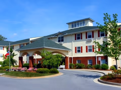 Exterior view of Creekside Pines Retirement Community building with a covered entrance, manicured landscaping, and a clear blue sky.