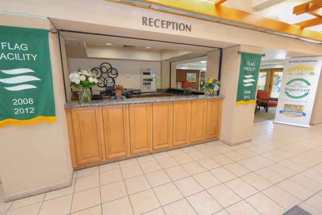 A reception desk with a granite counter and wood cabinets in a bright lobby, a receptionist seated behind the desk and banners on either side.