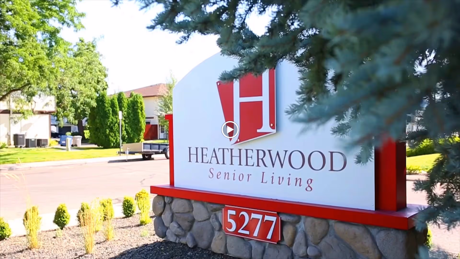 Entrance sign reading "Heatherwood Senior Living" with the address number 5277 set in a landscaped street view.