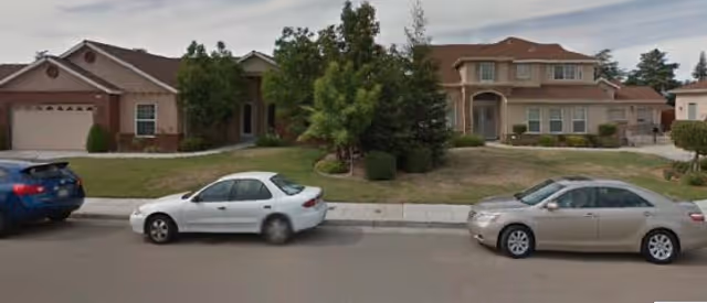 Street view of a residential care home with parked cars and a manicured front yard.