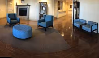 Regency at Livonia lounge with blue chairs, ottoman, and a fireplace.