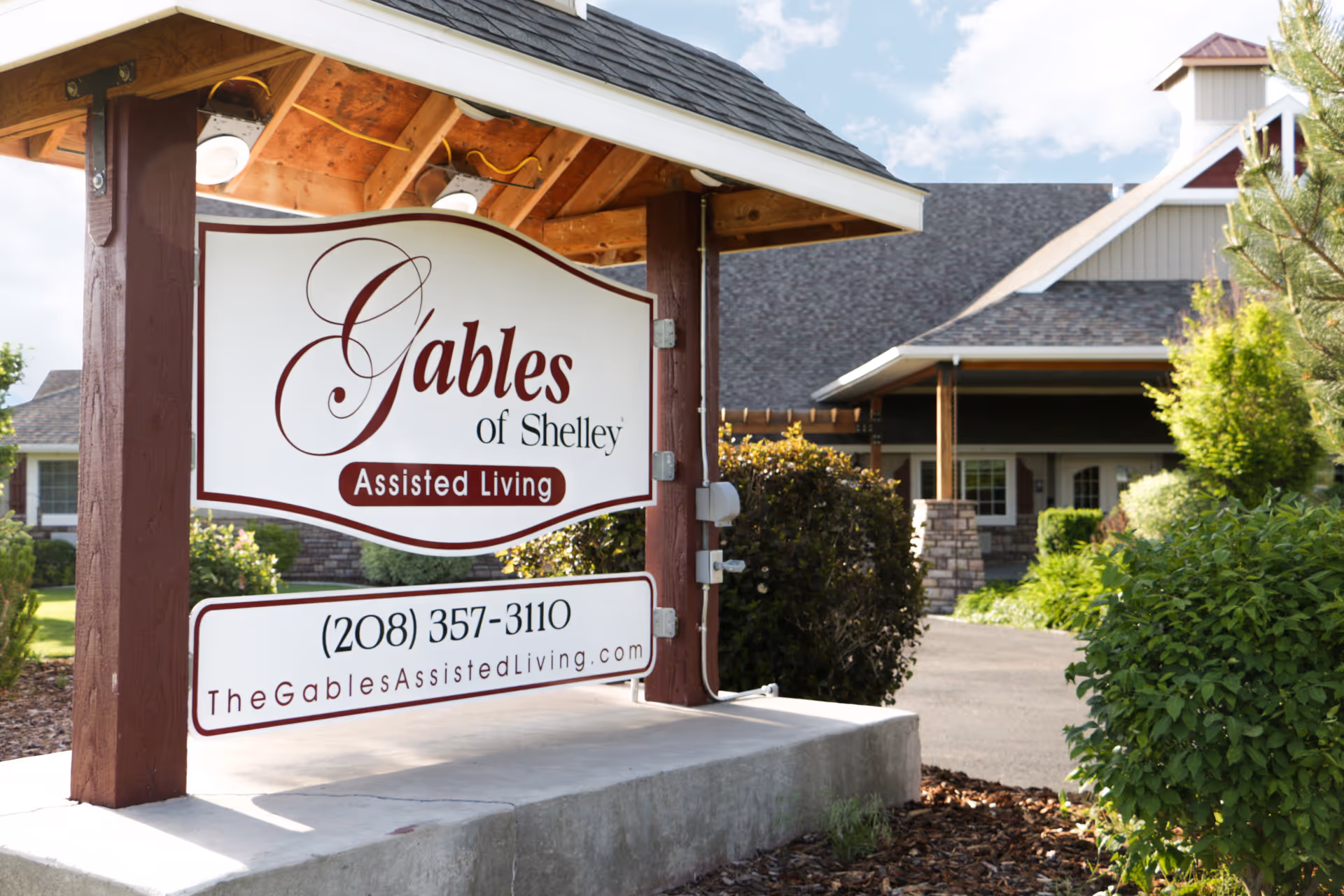 Outdoor wooden sign reading 'Gables of Shelley Assisted Living' with the facility building and landscaping in the background.