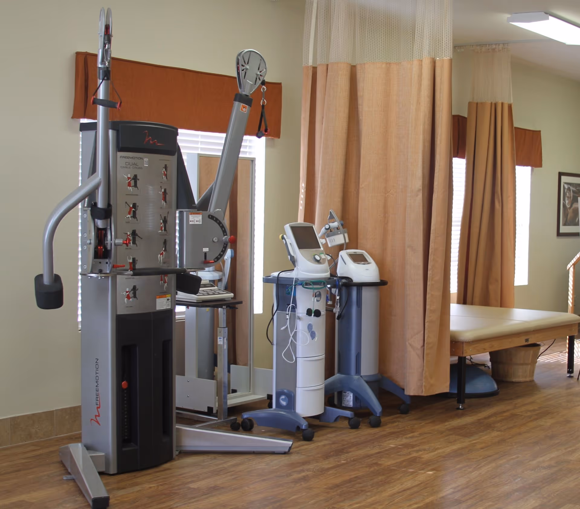 Physical therapy room with exercise equipment, medical devices on carts, a treatment table and privacy curtains.
