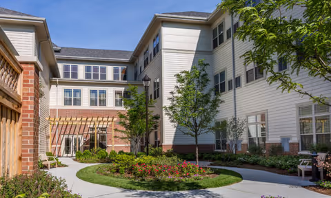 Landscaped central courtyard with a circular flower bed, walkways, benches, and a surrounding multi-story senior living building.