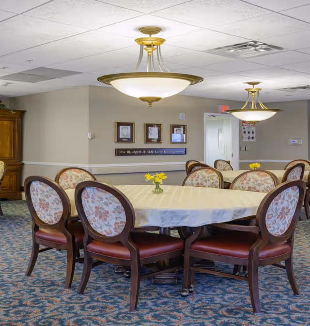 Round dining table with floral-upholstered chairs, small vases of yellow flowers, and hanging light fixtures in a dining room.