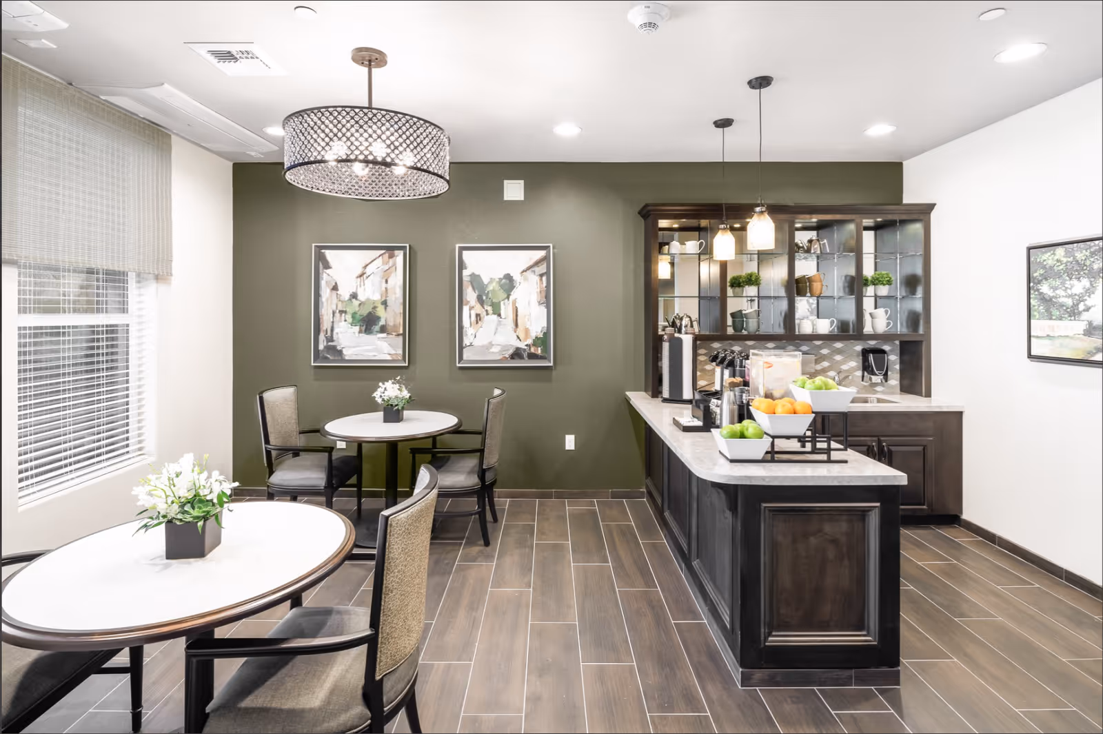 Bright dining area with round tables and chairs and a central coffee/snack bar against a green accent wall.