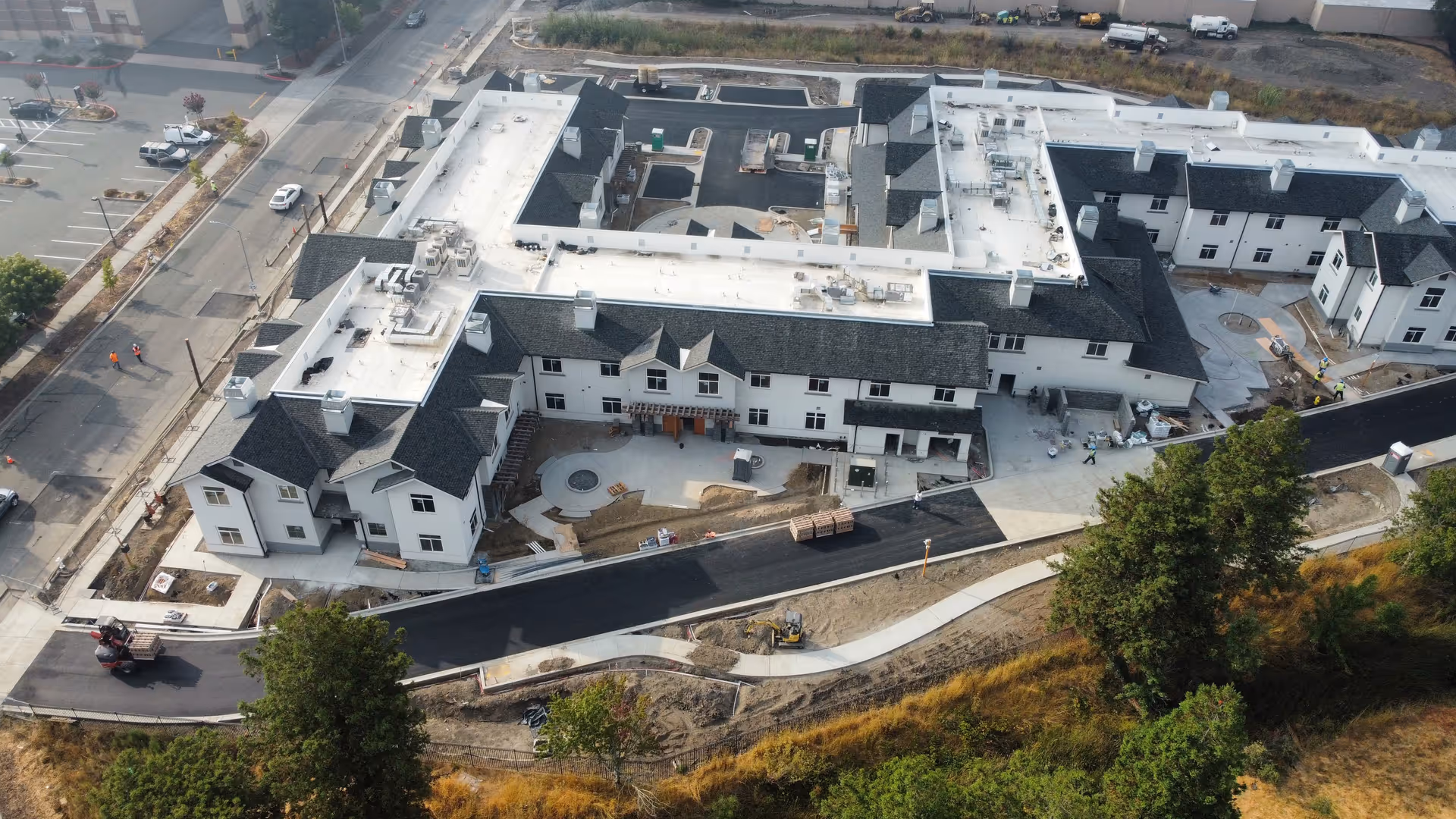 Aerial view of the Santa Rosa Hills Senior Living complex under construction, showing white buildings with dark roofs, paved driveways and surrounding landscaping.