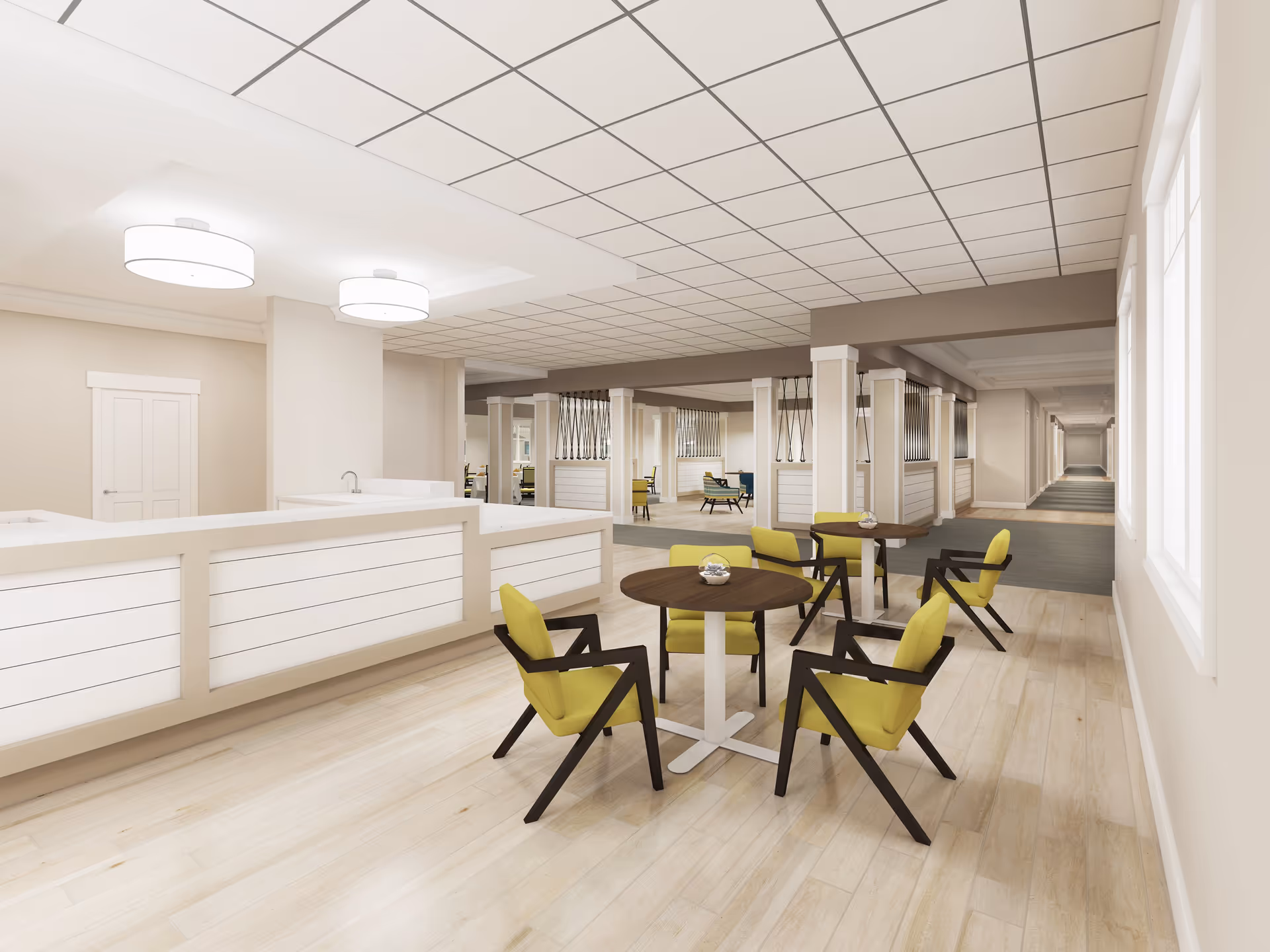 A spacious, modern interior common area with light wood flooring, white paneled walls, and a drop ceiling with grid pattern. There are round tables with green cushioned chairs arranged near a white reception or service counter. The area extends into a hallway and additional seating areas with similar furniture and decorative metal accents on partial walls.