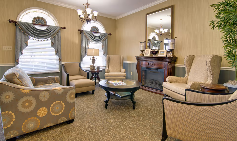 A cozy lounge with upholstered armchairs and a patterned sofa arranged around a round coffee table in front of a decorative fireplace.