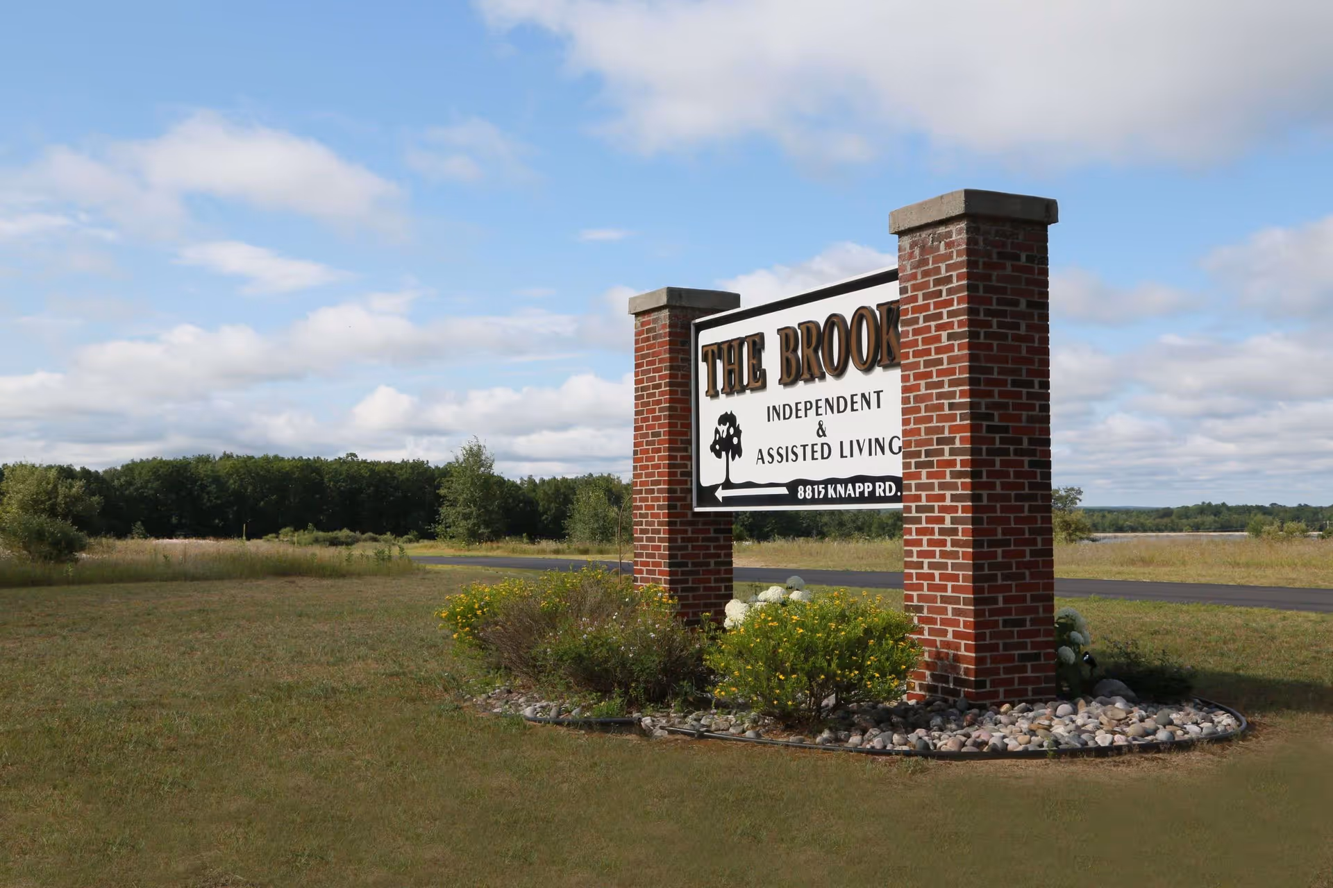 Brick-pillared roadside sign for The Brook independent and assisted living on a grassy lot.