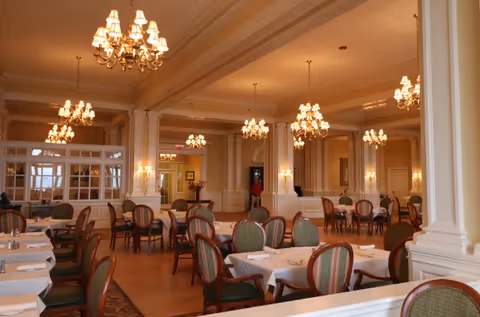 Spacious elegant dining room with multiple set tables and upholstered chairs beneath chandeliers.