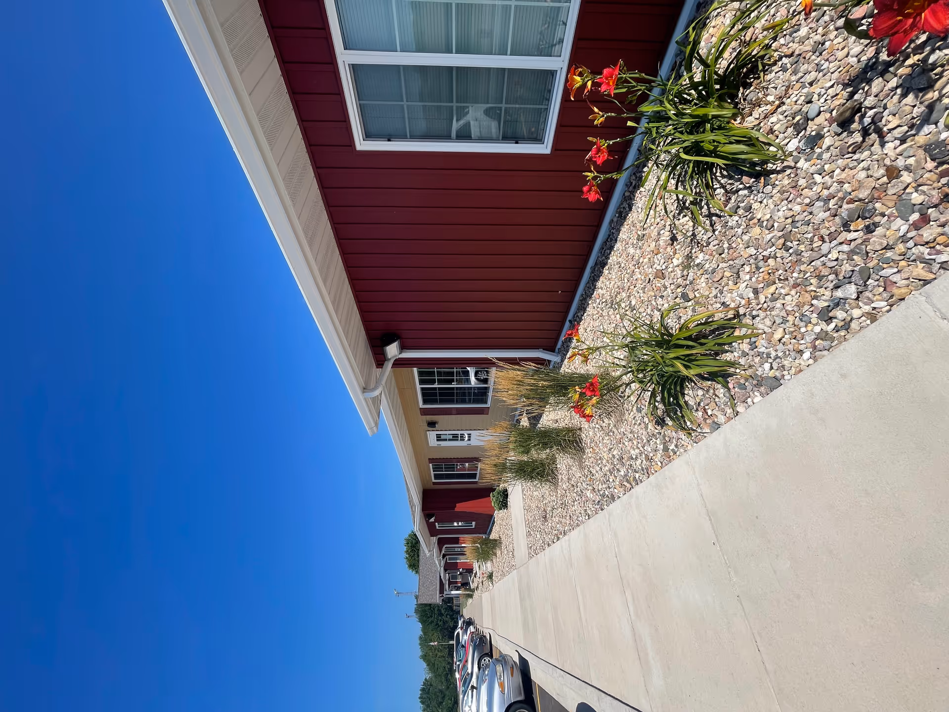 Front exterior of a red siding senior living building with a gravel walkway.