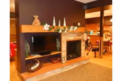 Common area with a TV and a fireplace set in a wooden entertainment unit, decorated mantle, and a dining area visible in the background.