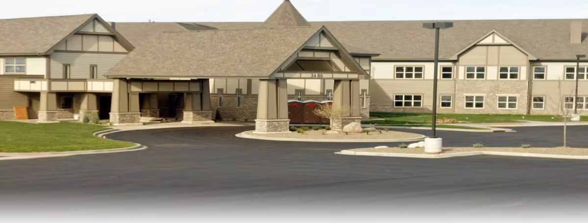 Exterior view of a large two-story building with a covered entrance and a paved driveway, surrounded by a well-maintained lawn and a few small trees.