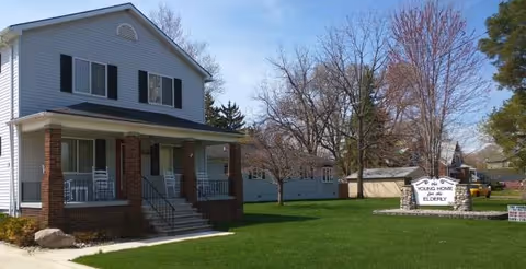 Two-story light-blue senior living home with a covered front porch and sign.