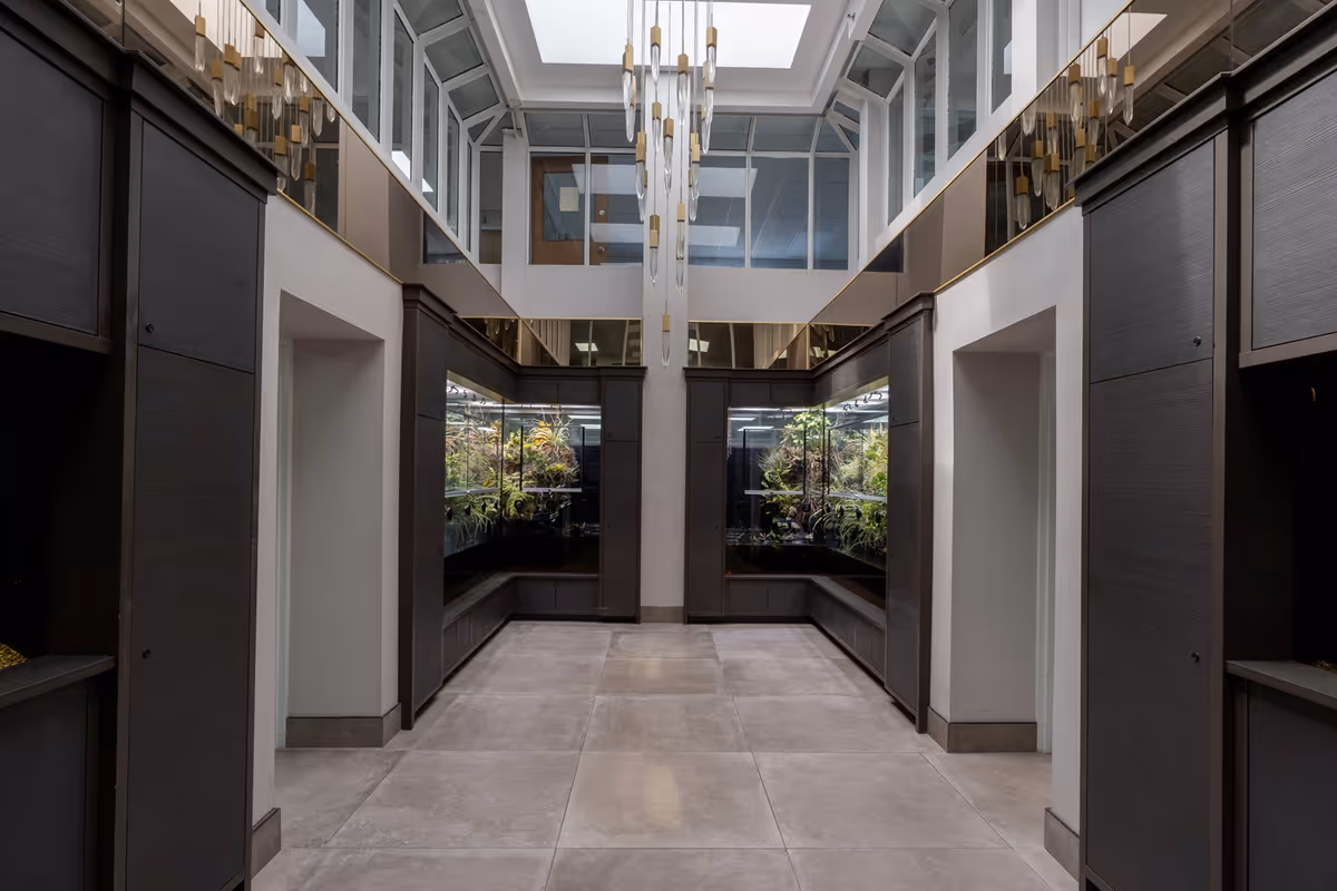 A modern, well-lit indoor atrium with glass walls, dark wood panels, and a central chandelier.