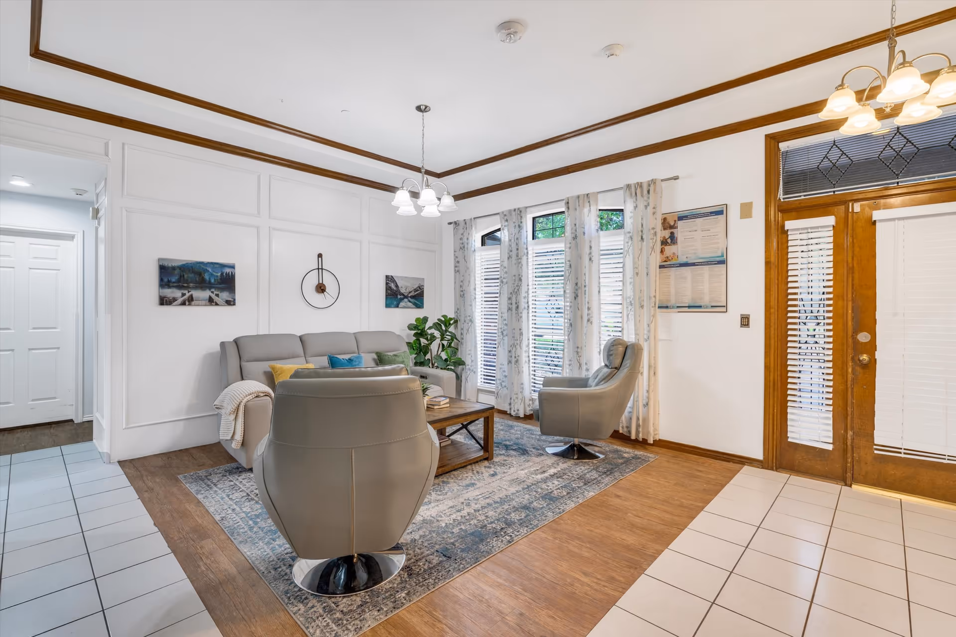 Well-lit common living room with sofas and armchairs arranged around a coffee table, area rug, and entry doors.