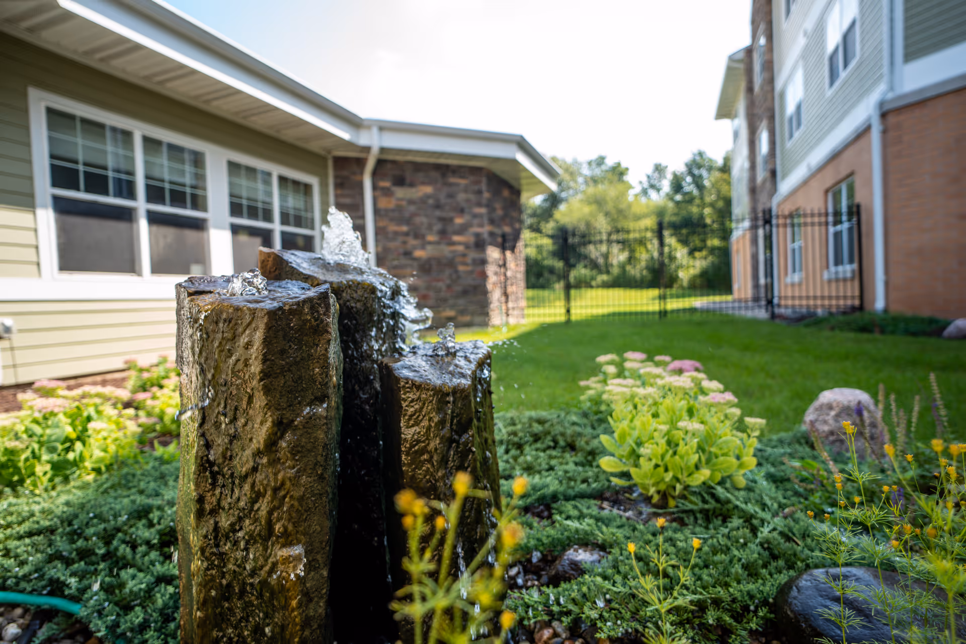 A stone water fountain in a landscaped courtyard between residential buildings.