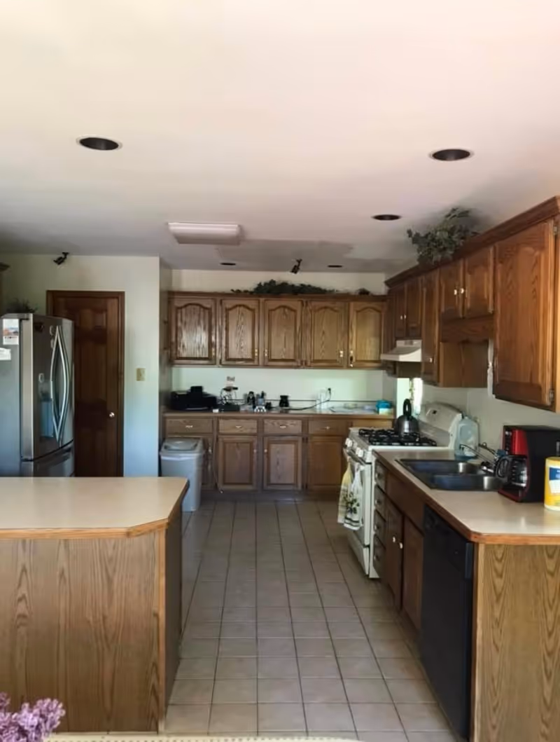 Galley-style kitchen with oak cabinets, a center island, tile floor, stainless refrigerator, stove, and sink.