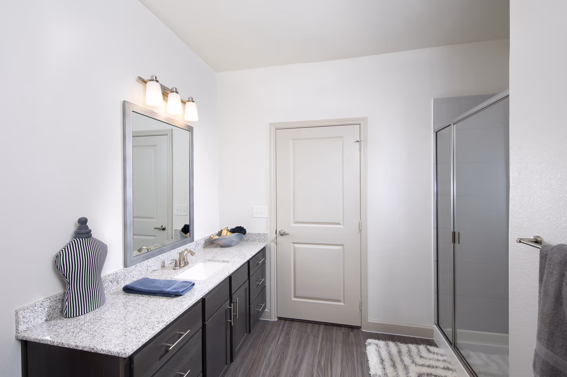 Bright modern bathroom with a long granite vanity, large mirror, sink and a glass-enclosed shower.