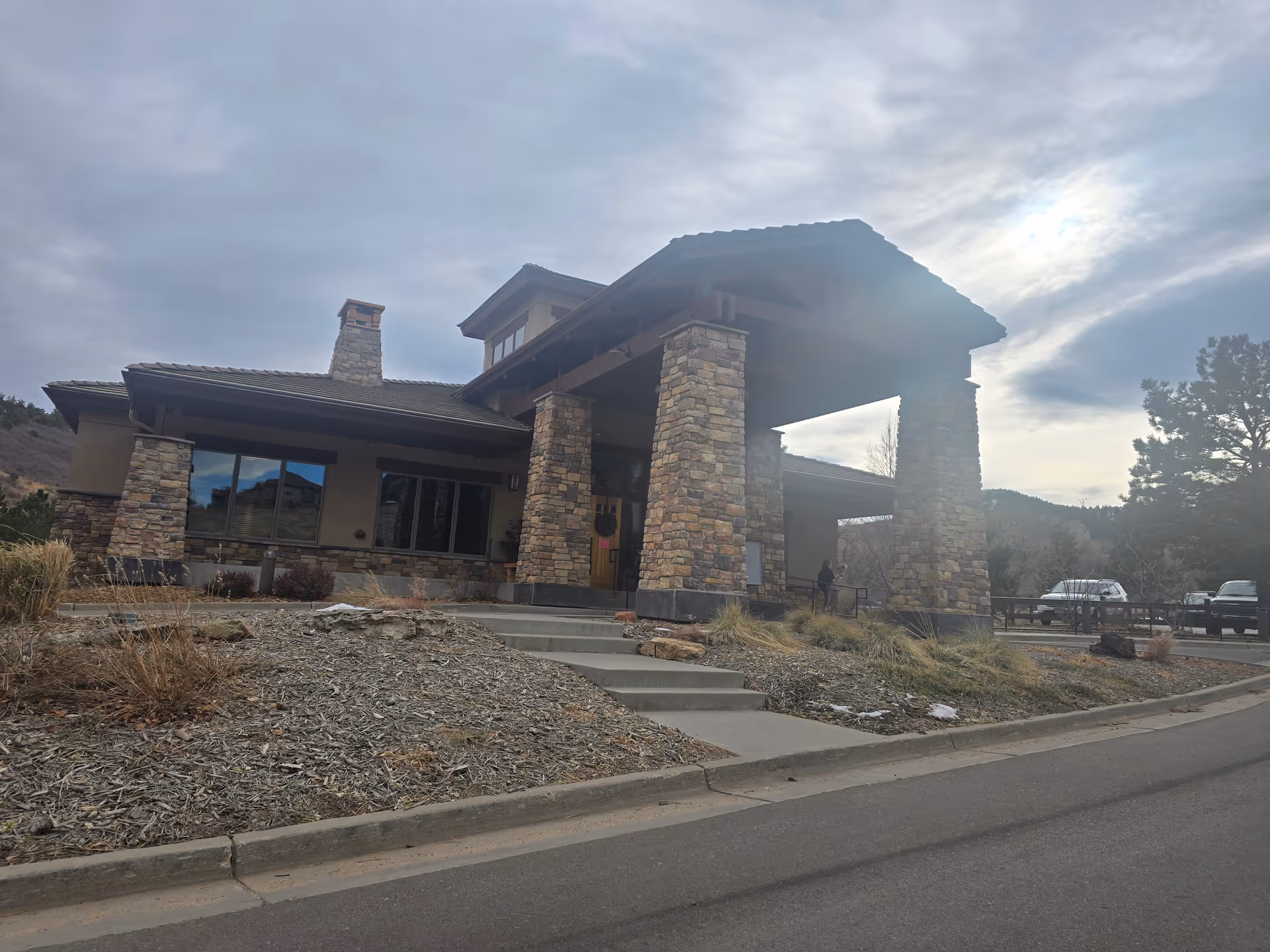 Front entrance of a stone-and-stucco building with a large covered entry supported by stone pillars and steps leading up.