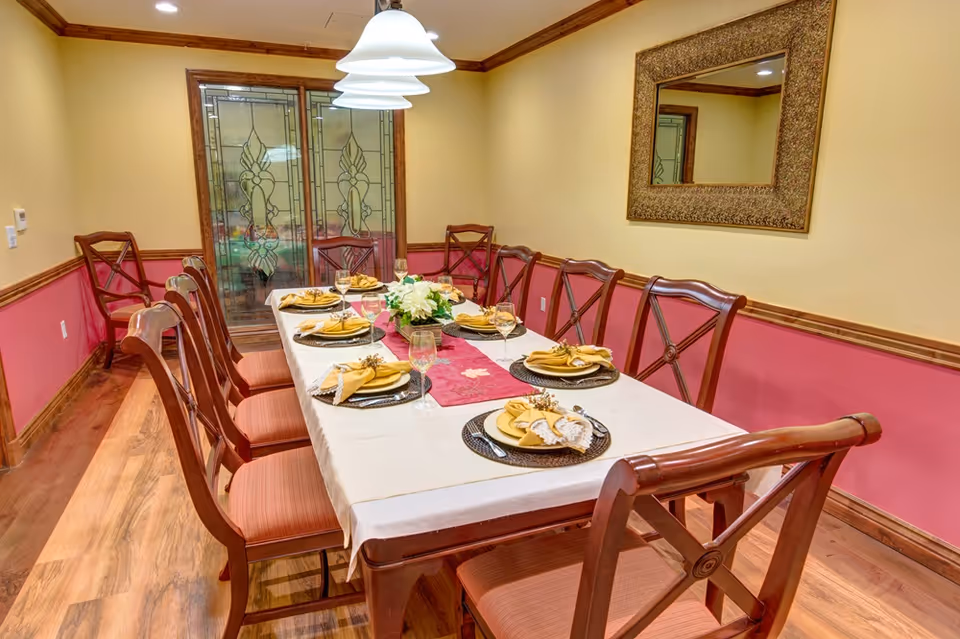 Dining room with a long set table, wooden chairs, pendant lights, and decorative stained-glass doors.