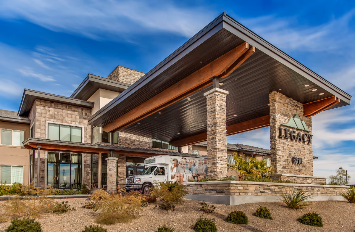 Stone-clad entrance canopy of the Legacy senior living facility with a shuttle van parked beneath.