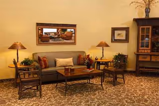 A cozy senior living lounge with sofa, chairs, coffee table, lamps, and a cabinet.