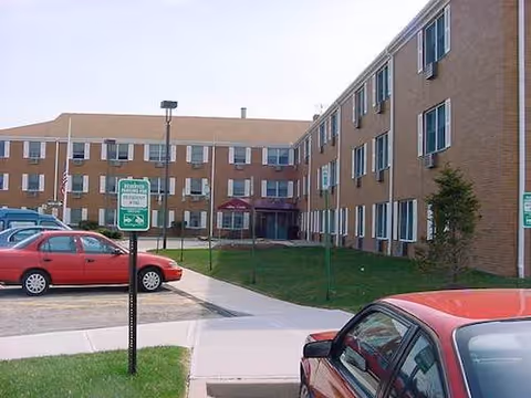 Exterior view of Allaire Crossing senior living building with parked cars.