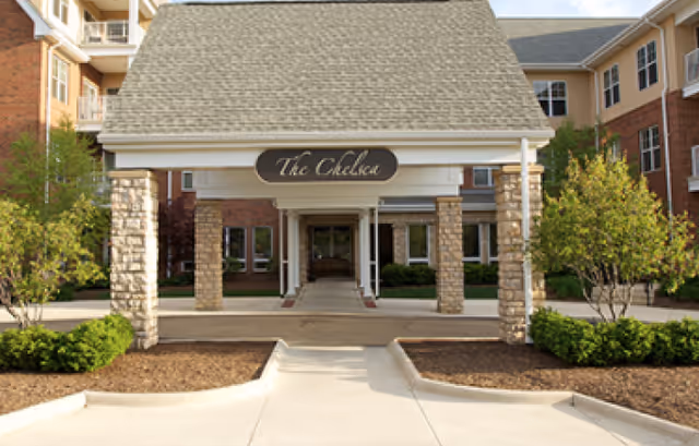 Covered entrance with stone pillars leading to the front doors of a brick senior living building.