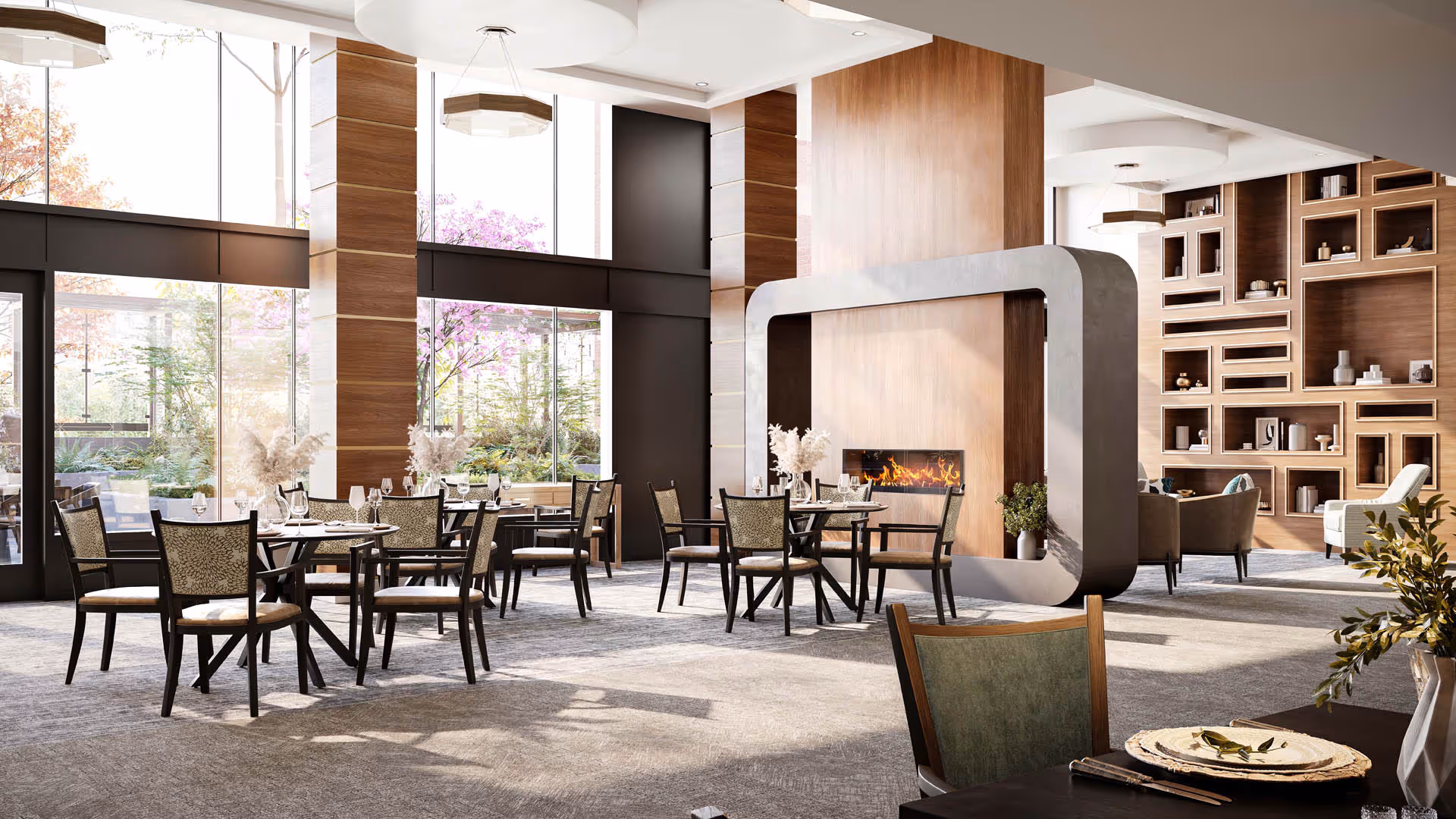 Spacious, sunlit communal dining room with round tables and chairs, a modern fireplace feature, tall windows, and built-in shelving.
