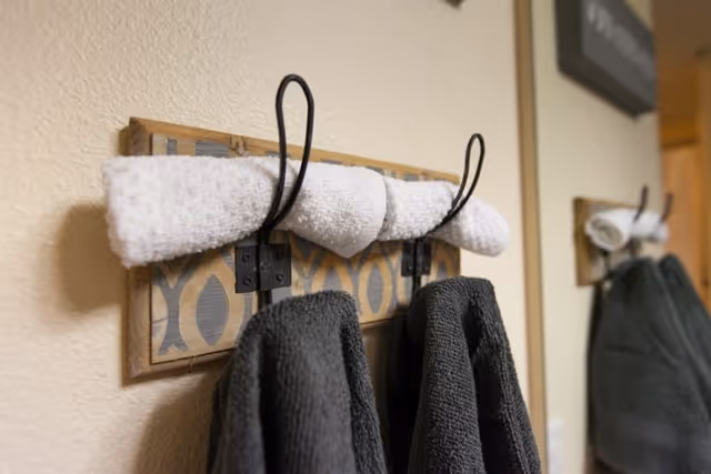 Wall-mounted towel rack holding rolled white hand towels and hanging dark gray bath towels on a beige wall.