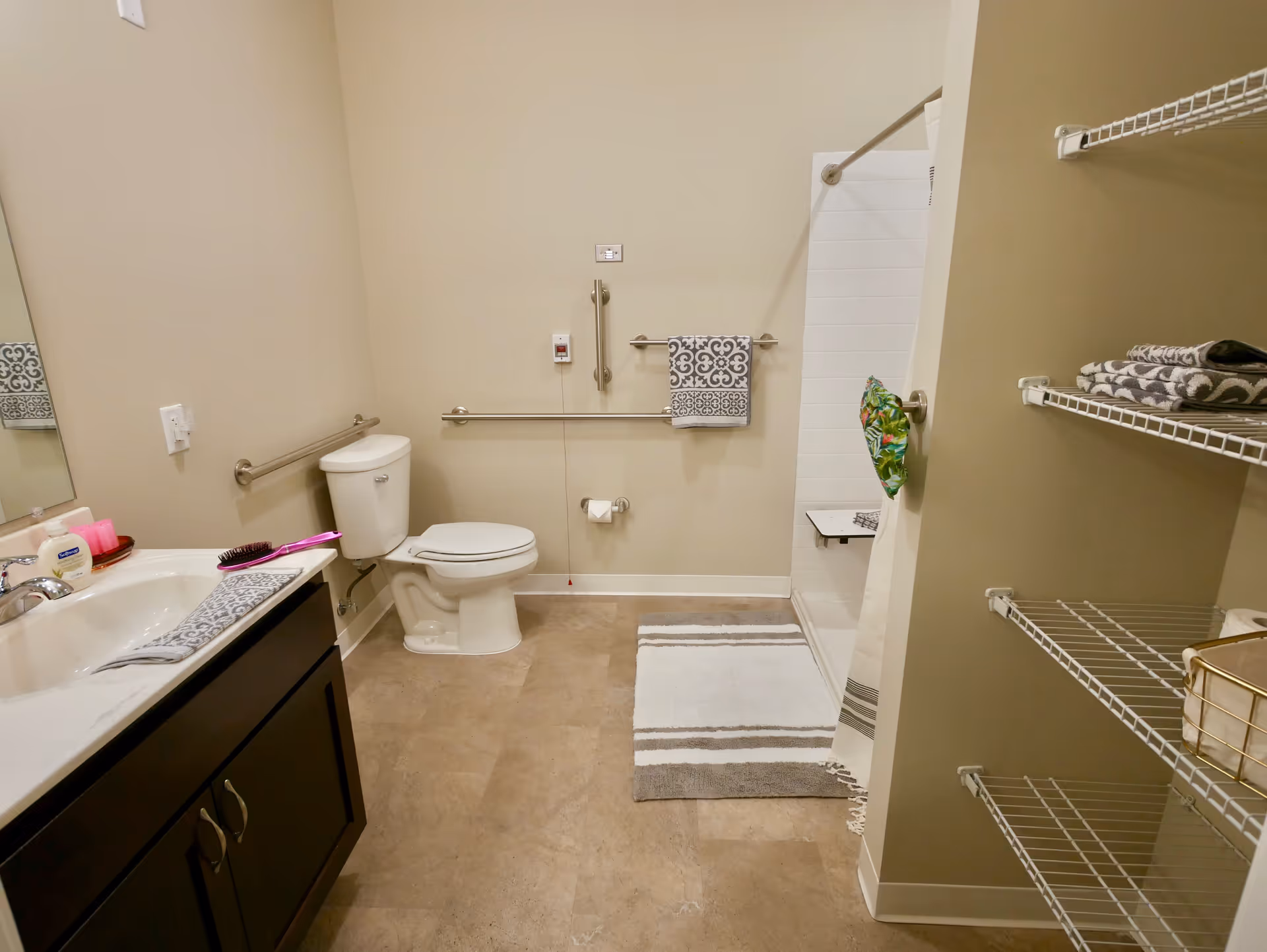 Accessible bathroom with toilet, sink and vanity, grab bars, walk-in shower, and shelving with towels.