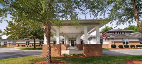 Front entrance with white columns and brick bases, surrounded by trees, and an American flag.